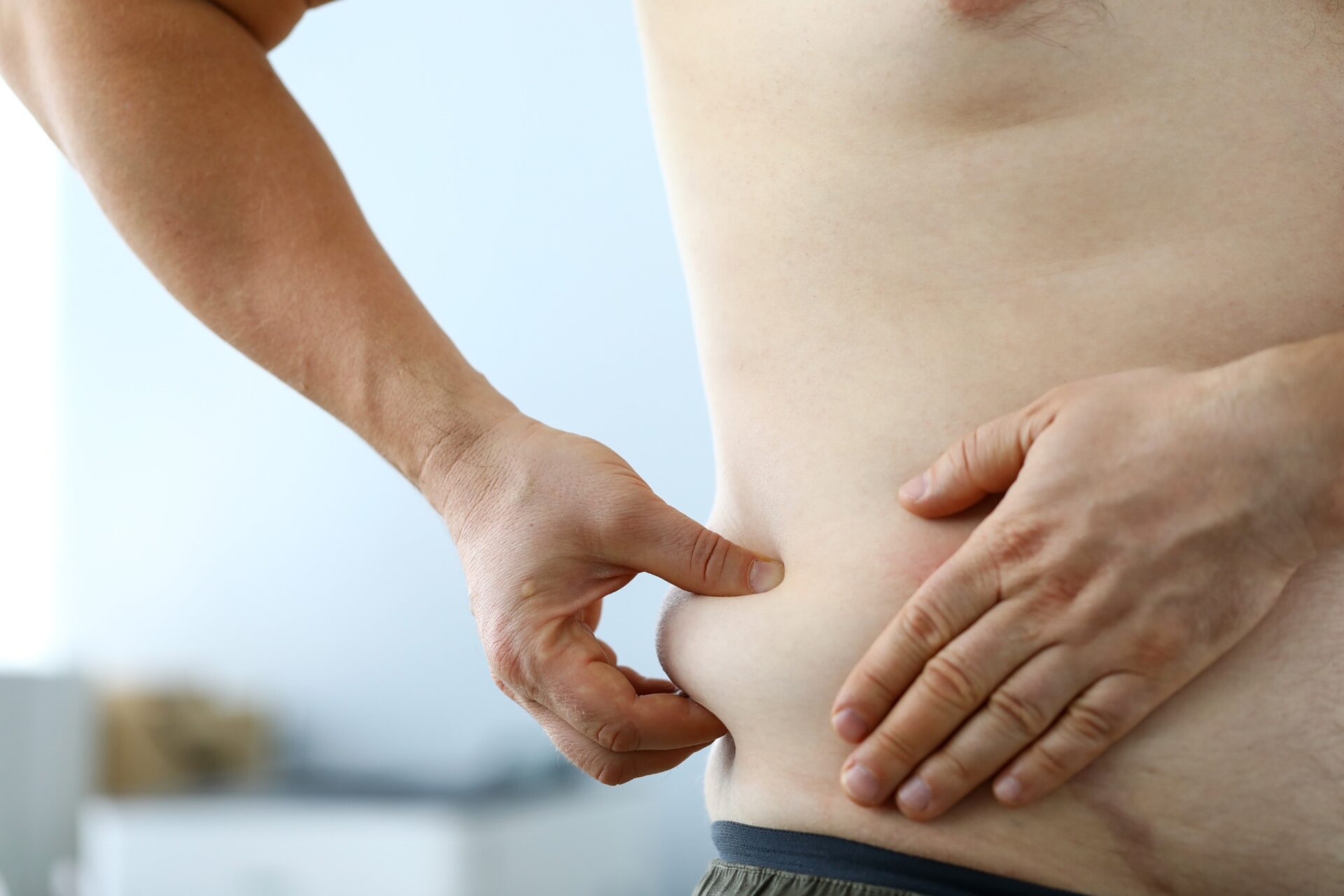 Close-up of male hand measuring thick waist to track down rate of getting plump and looking at overweight belly. Fat man preparing for training. Severe obesity and losing weight concept Close-up of male hand measuring thick waist to track down rate of getting plump and looking at overweight belly. Fat man preparing for training. Severe obesity and losing weight concept<br />