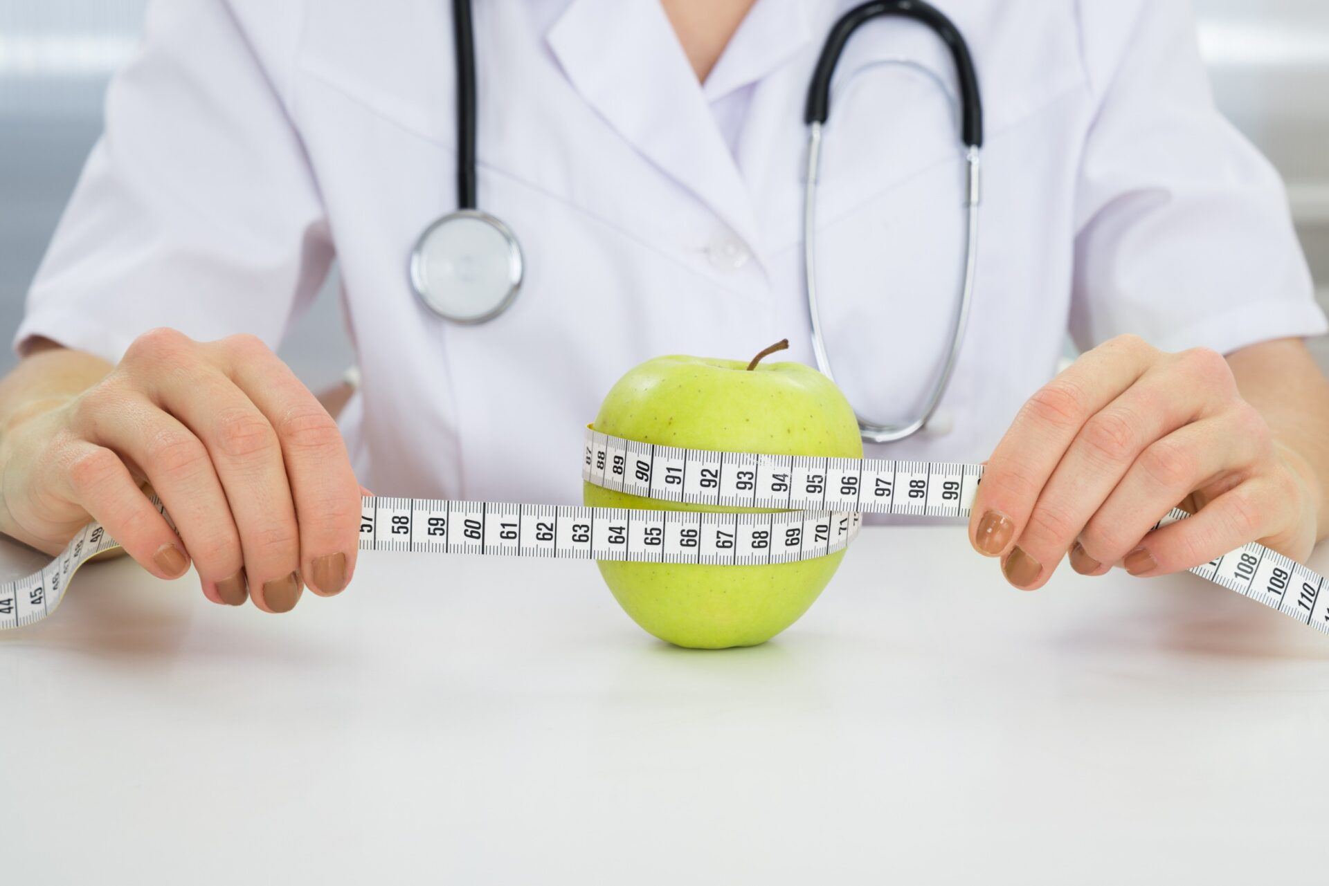 Close-up Of Dietician Measuring Green Apple With Measuring Tape Close-up Of Dietician Measuring Green Apple With Measuring Tape